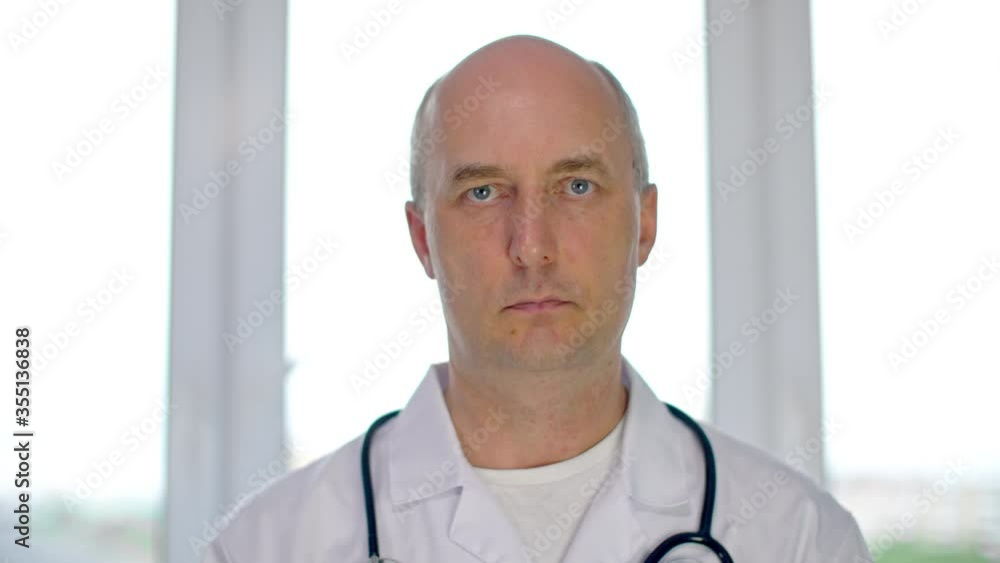 Serious male doctor swaying head and talking yes on window background in clinic. Portrait doctor saying yes while online consultation in medical office Serious male doctor swaying head and talking yes on window background in clinic. Portrait doctor saying yes while online consultation in medical office