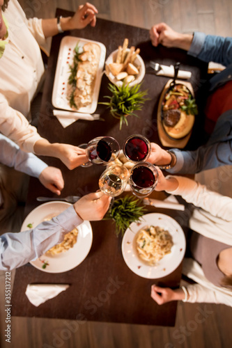 Four hands with red wine toasting over served table with food