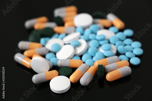 Pills and capsules, different medication scattered on a dark glass table. Concept of pharmacy, health care, vitamins