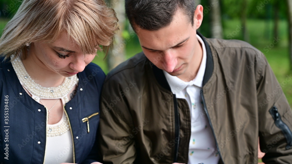 Relationship problems. A woman is talking to a man. Young couple are walking in the park using smartphones. The concept of family communication. Relationship problems. A woman is talking to a man. Young couple are walking in the park using smartphones. The concept of family communication.