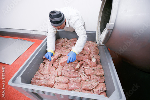 Horizontal view. A worker in the meat factory is applied and arranges pieces of meat marinated in spices, a food processing and production industry.