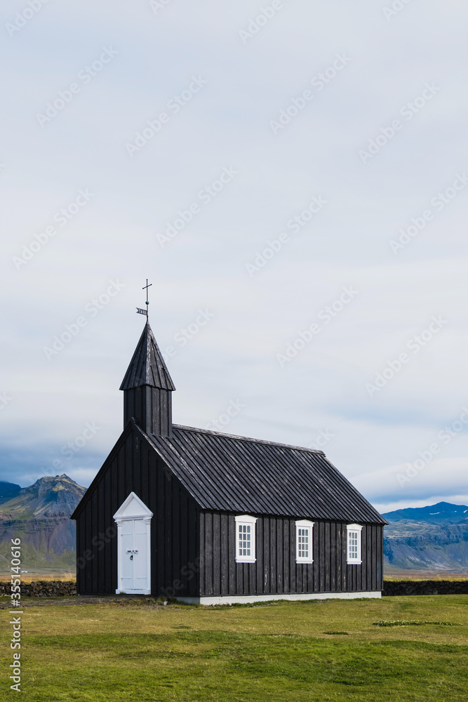 Black church in the meadow and field in Iceland. Icelandic scenic travel destination of religion. Christianity and religious concept. Postcard theme. Praying in chapel.Mountains on background.