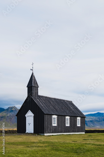 Black church in the meadow and field in Iceland. Icelandic scenic travel destination of religion. Christianity and religious concept. Postcard theme. Praying in chapel.Mountains on background.