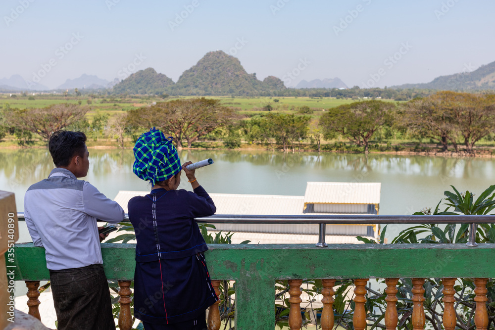 Obraz premium Young couple dressed in traditional shan clothes: scarf on the head, traditional longyi. Landscape in the surroundings of the Kyaut Ka Latt pagoda. Hpa An, Myanmar - Burma, Southeast Asia
