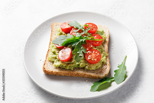 Avocado rye bread toast with cherry tomatoes and arugula on bright background.