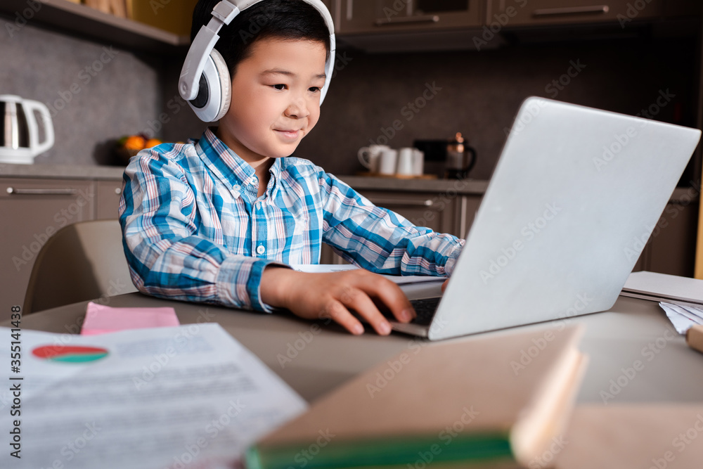 smiling asian boy studying online with books, laptop and headphones at home during quarantine smiling asian boy studying online with books, laptop and headphones at home during quarantine