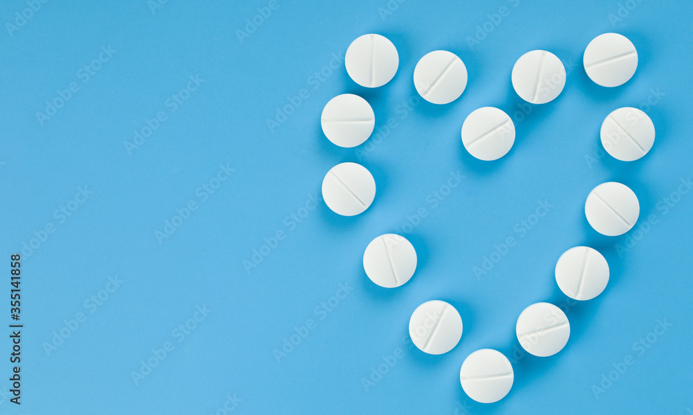 White pills laid out in the form of a heart on a blue background close-up. White pills laid out in the form of a heart on a blue background close-up.