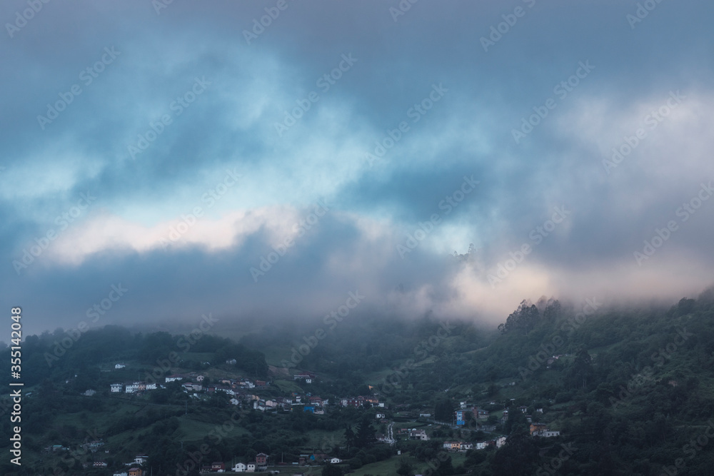 Landscape of cloudy mountains and a small town surrounded by forests and meadows