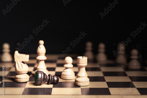 Closeup  Black pawn lie on chessboard and surrounded by white knight  bishop  rook and pawn. Other chess pieces in background. Authority  Black Lives Matter and human rights concept