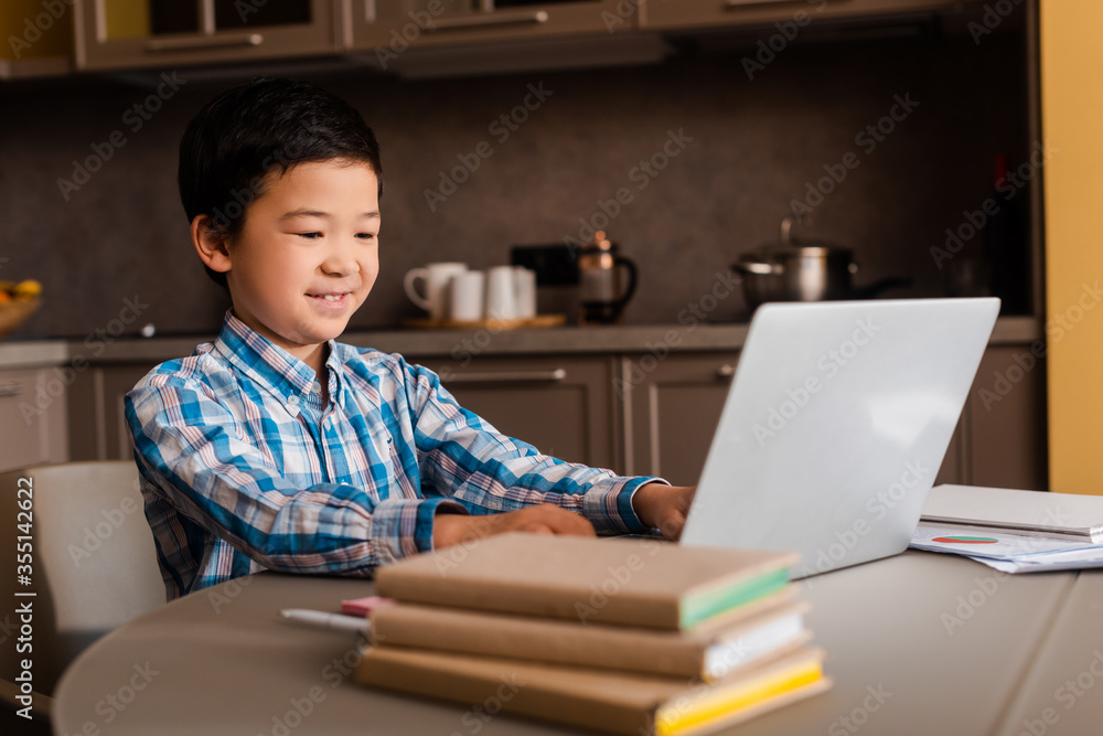 smiling asian boy studying online with laptop and books at home during quarantine smiling asian boy studying online with laptop and books at home during quarantine