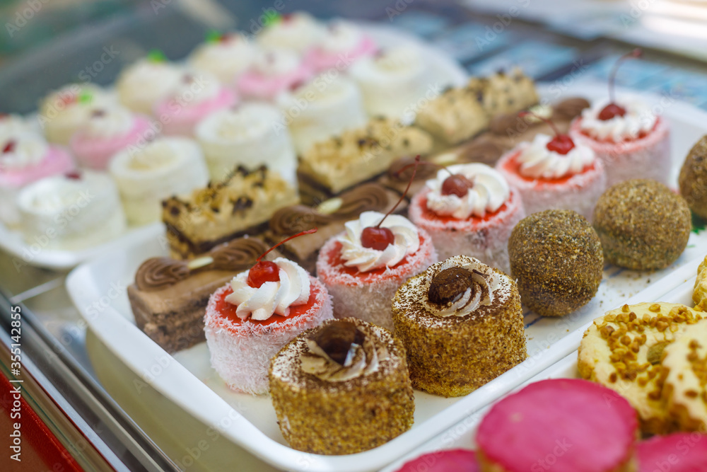 Sweet lush cakes lie on trays in a shop window. Side view, focus on the foreground. Sweet lush cakes lie on trays in a shop window. Side view, focus on the foreground.
