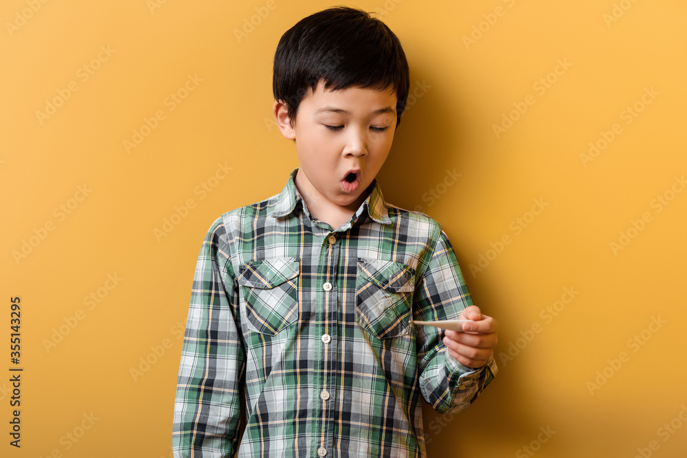 shocked asian boy holding thermometer on yellow shocked asian boy holding thermometer on yellow