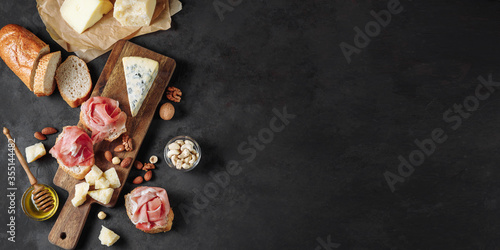 Appetizer, aperitif or snack table with prosciutto, cheese, nuts, bread and honey.
