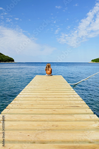 child sitting on ooden bridge in frontof the sea photo