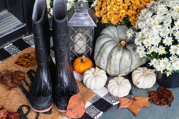Rain boots on the front porch decorated for autumn with heirloom gourds,  white pumpkins, mums and buffalo plaid welcome mat for an inviting atmosphere.