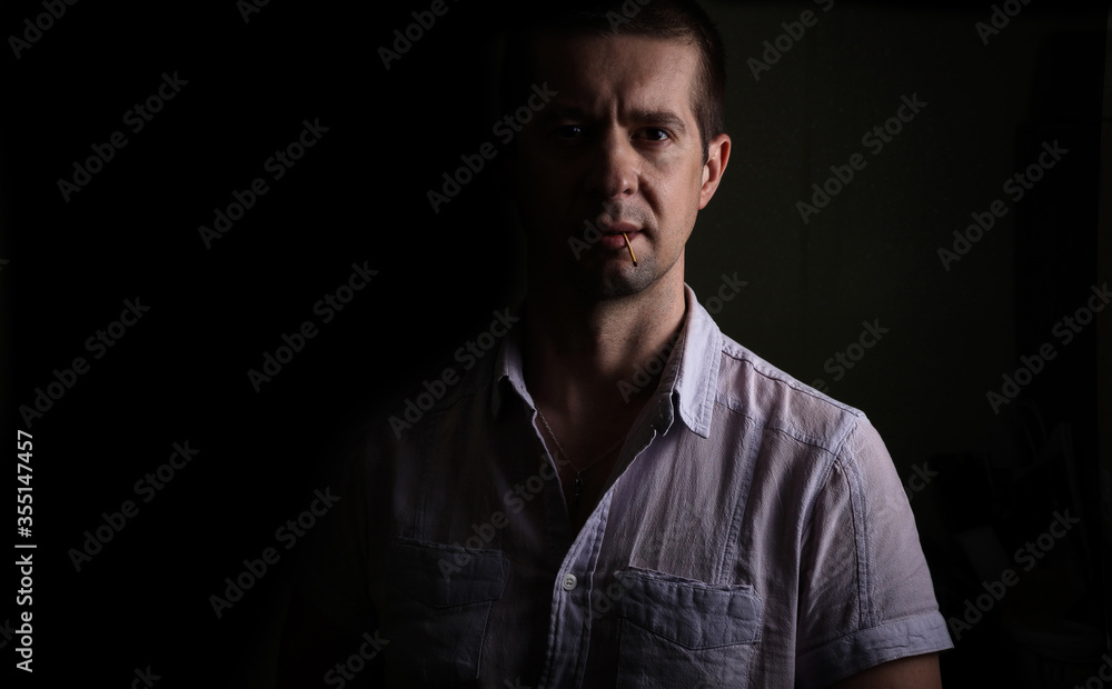 Confident brazen man holds a match in his teeth, in a short-sleeved shirt, looking at the camera, isolated, on black Confident brazen man holds a match in his teeth, in a short-sleeved shirt, looking at the camera, isolated, on black