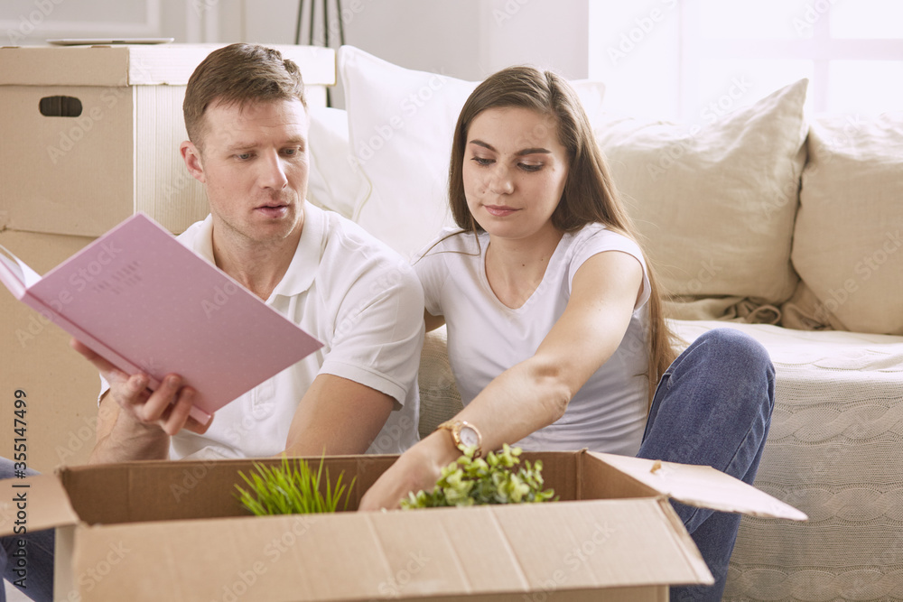 Portrait of happy couple looking at laptop computer together sitting in new house, surrounded with boxes Portrait of happy couple looking at laptop computer together sitting in new house, surrounded with boxes