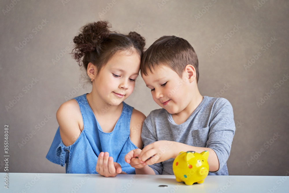 Fototapeta premium two children count money and put it in a piggy Bank
