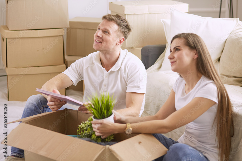 Portrait of happy couple looking at laptop computer together sitting in new house, surrounded with boxes Portrait of happy couple looking at laptop computer together sitting in new house, surrounded with boxes