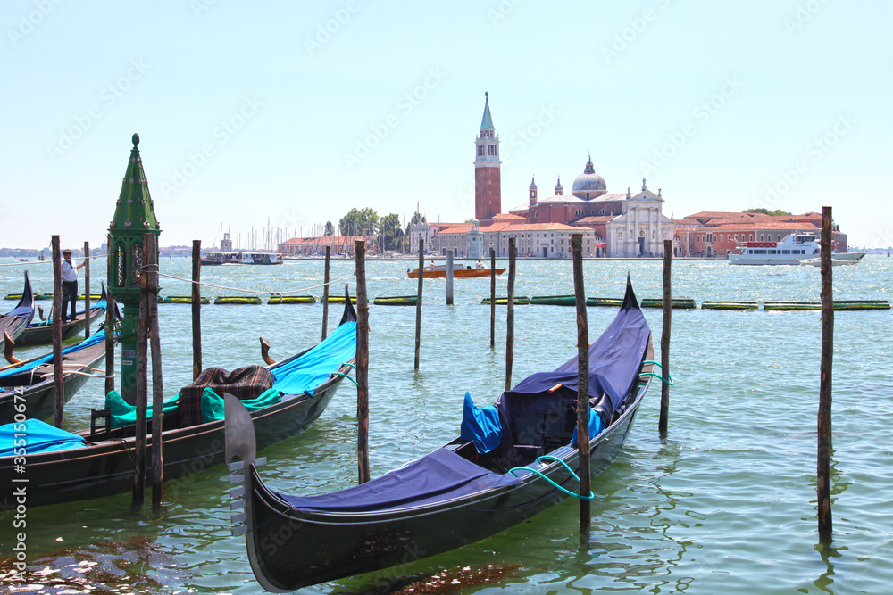 A view of several gondolas moored between wooden posts with the Church of San Giorgio Maggiore in the background.