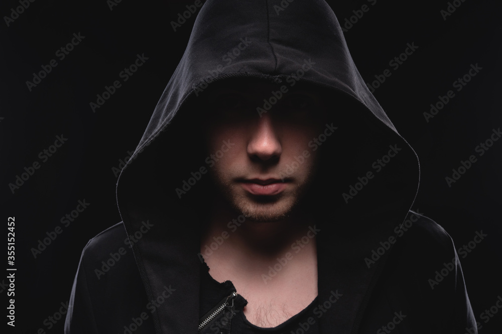 Close-up portrait of a courageous man in a deep dark hood on a black background. The concept of secrecy of secrets and people hiding from the government. Hackers and thieves. Low key Close-up portrait of a courageous man in a deep dark hood on a black background. The concept of secrecy of secrets and people hiding from the government. Hackers and thieves. Low key