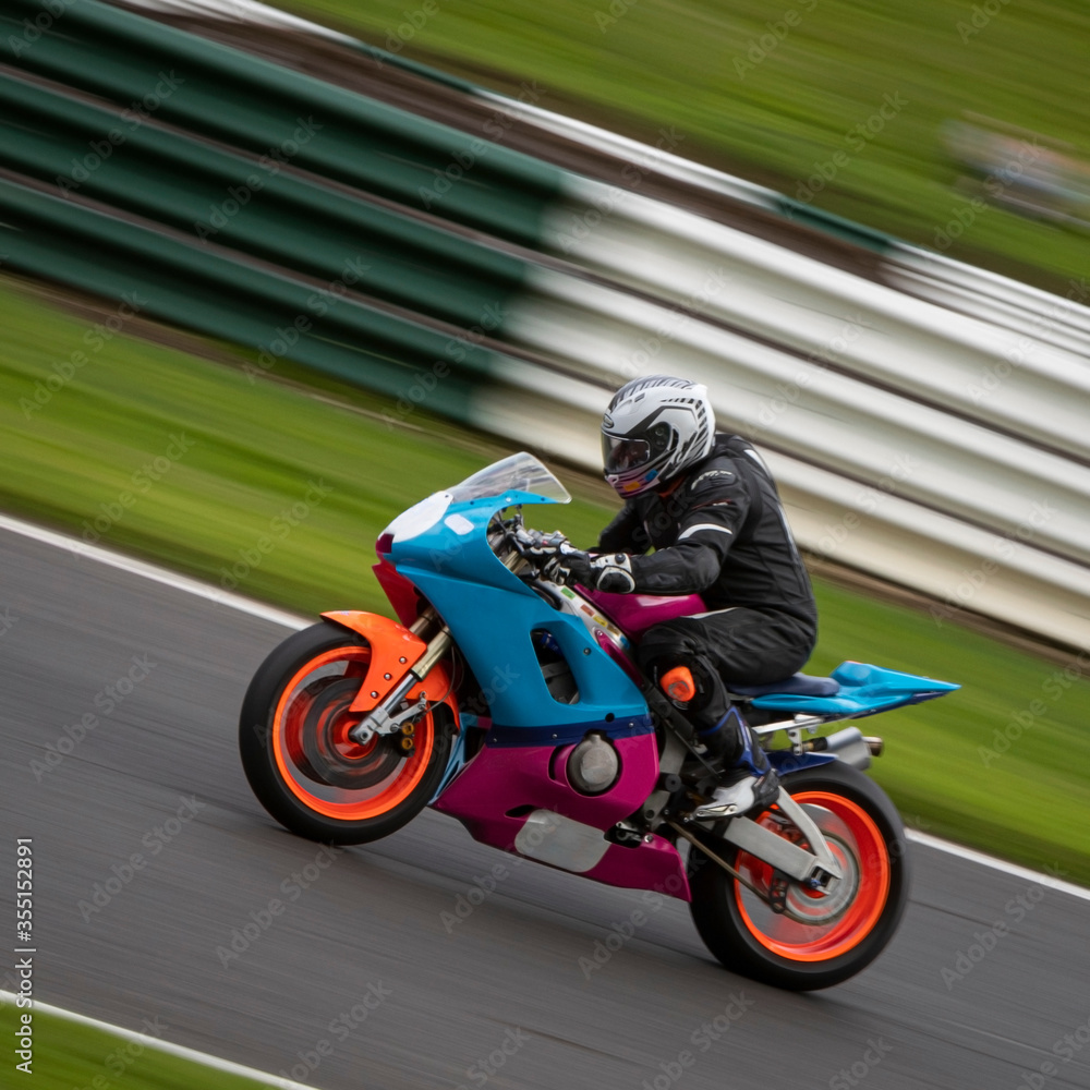 A panning shot of a blue and pink racing bike as it circuits a track
