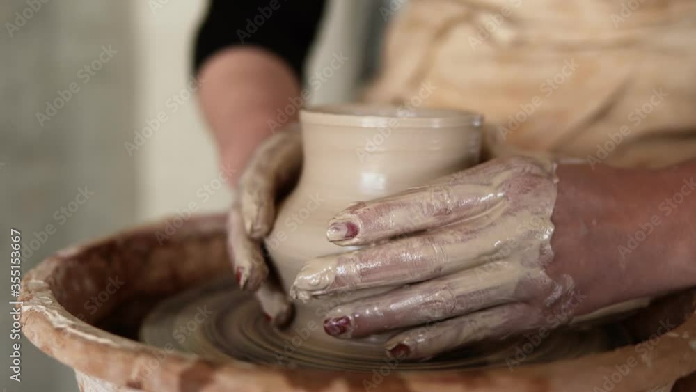 Close-up of potter's dirty hands working with wet clay on a pottery wheel making a vase in a workshop. Unrecognizable female person forming product Close-up of potter's dirty hands working with wet clay on a pottery wheel making a vase in a workshop. Unrecognizable female person forming product