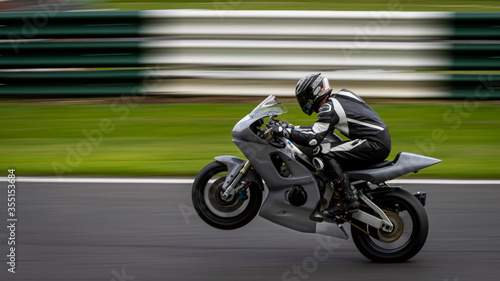 A panning shot of a grey racing bike on one wheel as it circuits a track