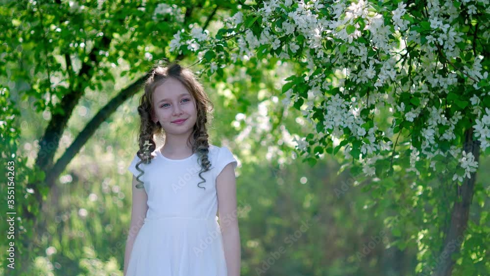 Smiling curly girl portrait in sunny garden on blooming fruit trees background. Happy girl model posing in blooming spring orchard Smiling curly girl portrait in sunny garden on blooming fruit trees background. Happy girl model posing in blooming spring orchard