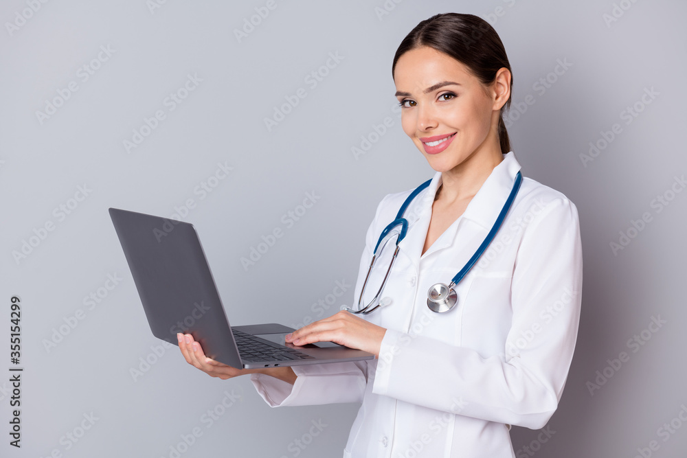Photo of professional family doc lady browsing modern technology notebook call covid sick patients online video examination wear stethoscope white lab coat isolated grey color background Photo of professional family doc lady browsing modern technology notebook call covid sick patients online video examination wear stethoscope white lab coat isolated grey color background