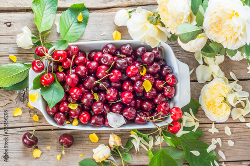 Fresh cherries in a bowl and roses on the wooden table.