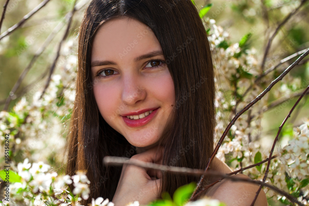 Pretty teen girl are posing in garden near blossom cherry tree with white flowers