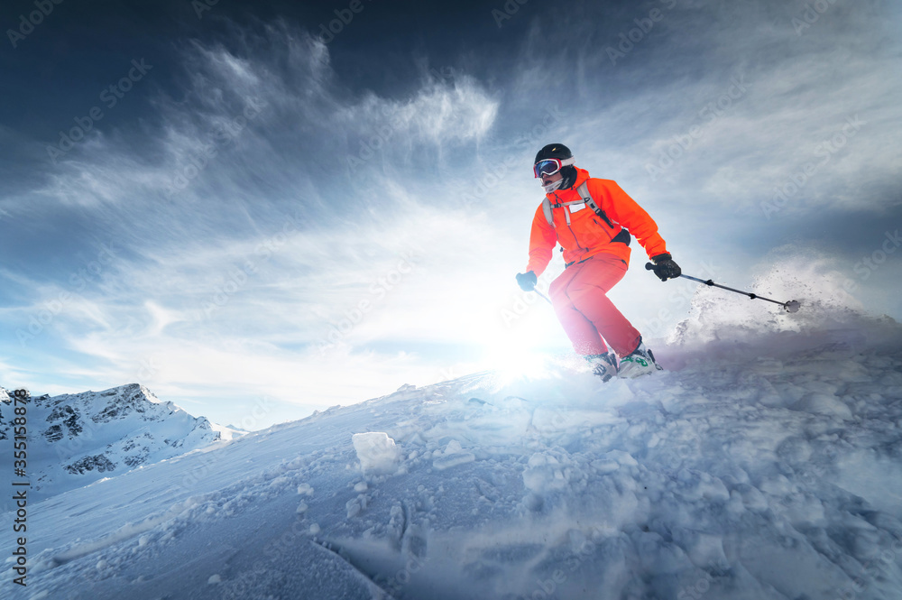Skier rides on a snowy slope on a sunny day at sunset against the backdrop of the mountains. The concept of winter skiing