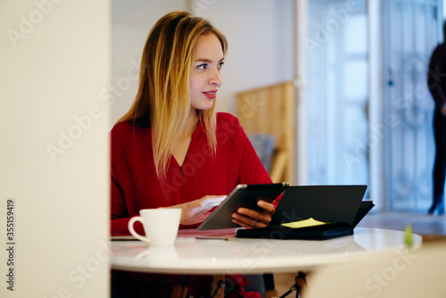 Pensive attractive blonde businesswoman checking email box via touchpad while planning working schedule ,professional marketing expert browsing information for project on device connected to wifi