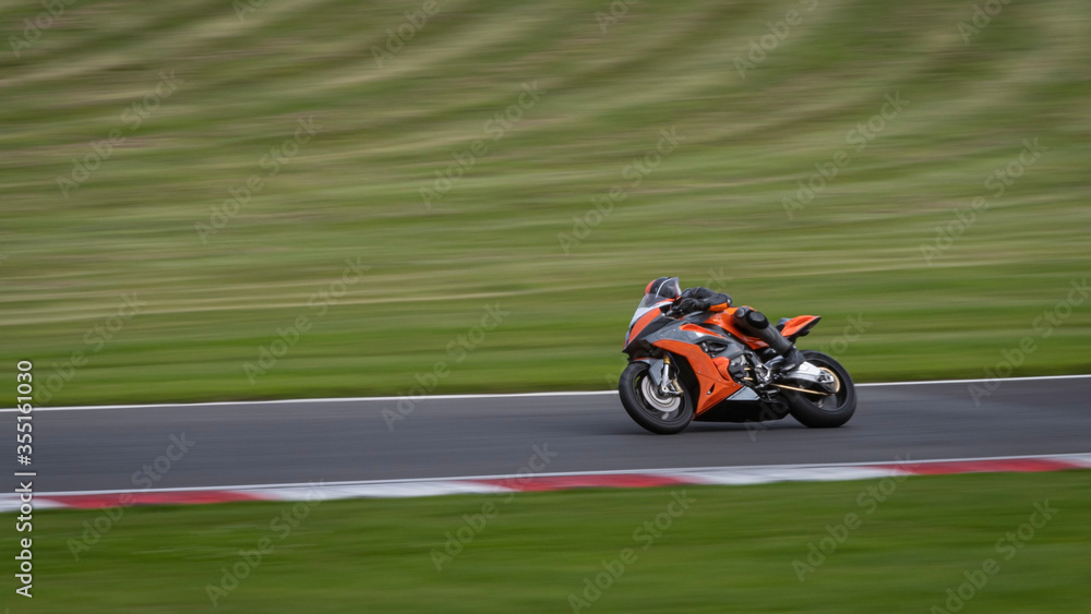 A panning shot of an orange racing bike cornering on a track