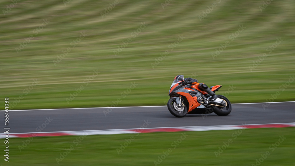 A panning shot of an orange racing bike cornering on a track A panning shot of an orange racing bike cornering on a track