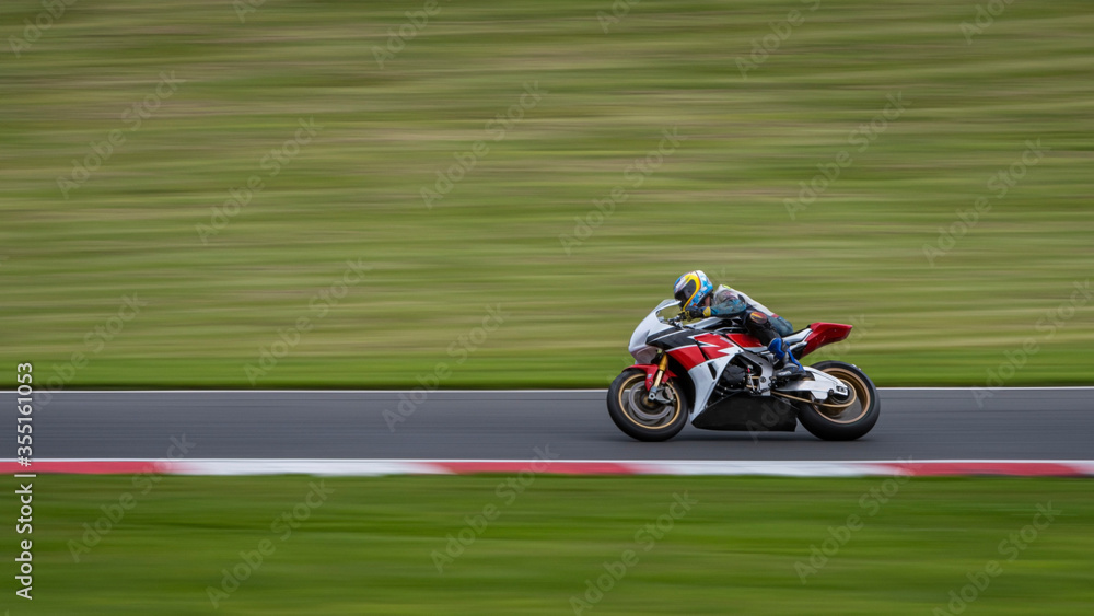 A panning shot of a white and red racing bike cornering on a track