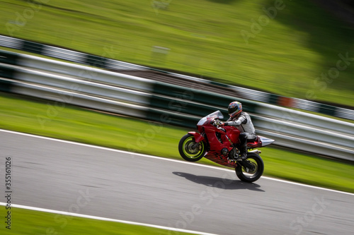 A panning shot of a red racing bike on one wheel as it circuits a track