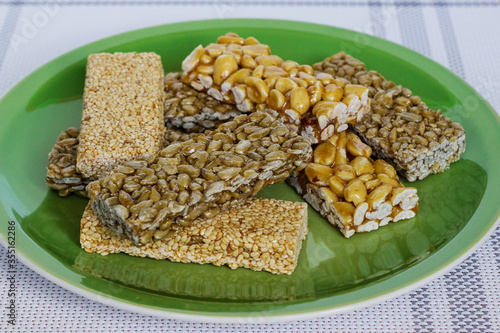 Kozinaki with seeds, nuts, sesame seeds and honey in a green plate. Useful snacks. Fitness diet food, nutritious snack, sesame halva, energy bar. Tasty and appetizing charge of energy. Close-up photo