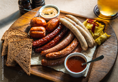 Hunting sausages on a wooden board on the table. Ketchup and mustard and brown bread next to the sausages.