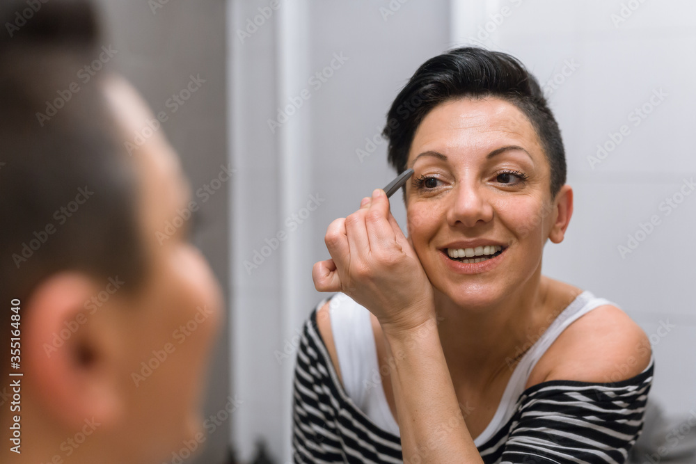 woman picking eyebrows in her bathroom woman picking eyebrows in her bathroom