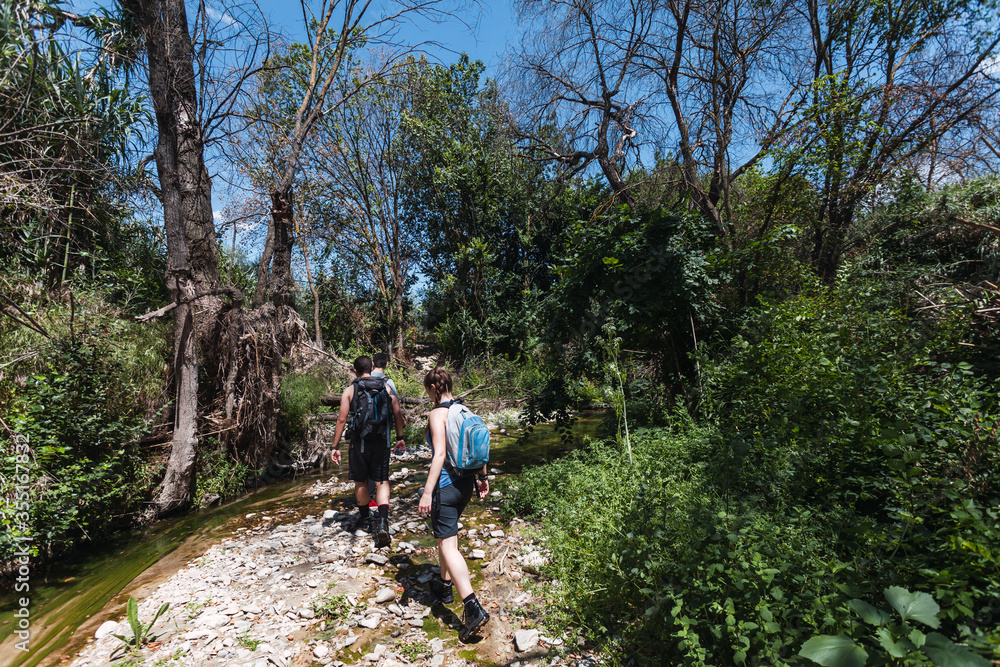 Small group of young tourists walking inside a river with little flow inside a forest in Spain in spring. Selective focus.