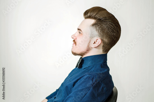 Young man with pompadour haircut, dressed in blue shirt with a serious face. side view hair for barbershop photo