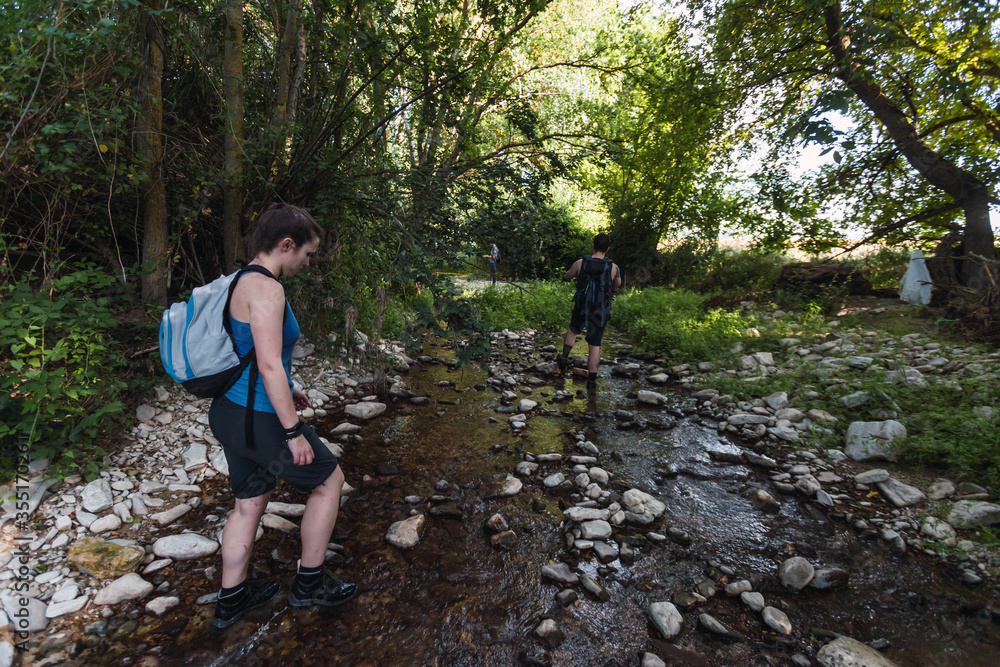 Small group of young tourists walking inside a river with little flow inside a forest in Spain in spring. Selective focus.