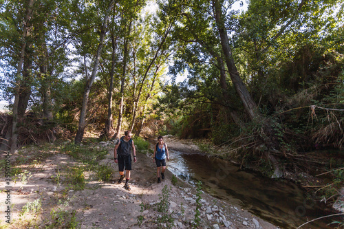 Small group of young tourists walking inside a river with little flow inside a forest in Spain in spring. Selective focus.