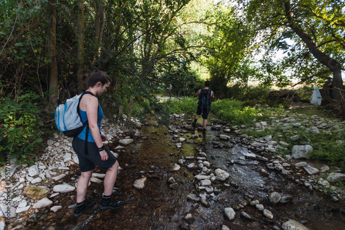 Small group of young tourists walking inside a river with little flow inside a forest in Spain in spring. Selective focus.