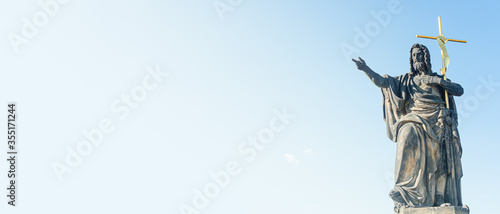 Banner with ancient statue of a saint monk with a cross at the Charles Bridge in Prague at blue sky and copy space for text, Czech Republic, summer, closeup