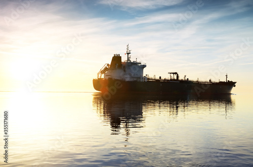 Large black tanker sailing in an open sea from the Europort at sunset. Colorful evening clouds. Symmetry reflections on the water. Rotterdam, Netherlands. Logistics, global communications theme photo