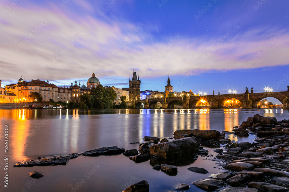 Towers and Charles bridge in the morning with moving clouds and stars. Stones on the foreground. Long exposure.