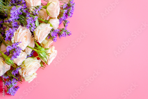 a bouquet of cream roses and bright purple flowers in full bloom on a pink background with space for text. greeting card